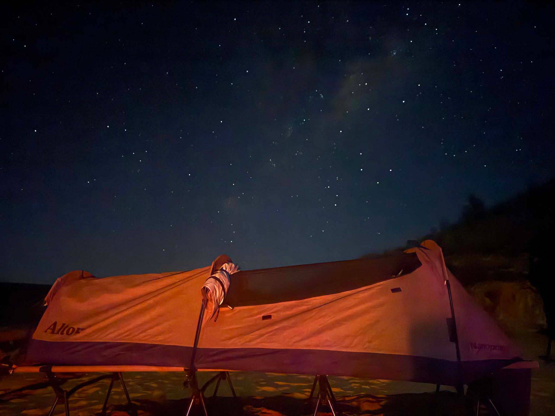 Firelit swag on a raised stretcher beneath a star-filled night sky